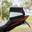 A motorcycle rear luggage bag with a black and light gray design and red zipper pulls, mounted on the back of a red motorcycle in an outdoor setting.
