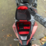 A top-down view of a motorcycle storage compartment with its lid open, showing a red and black mesh organizer inside. 