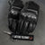 Black motorcycle gloves with a keychain labeled 'Lactose Tolerant' on a gray background